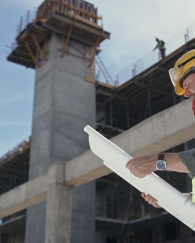 A builder reading a blueprint at a construction site. A mature man working on an architecture project. An engineer looking at a plan